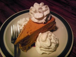 Slice of pumpkin cheesecake with whip topping on a plate with a fork.