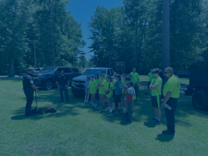 Group of summer campers wearing yellow t-shirts at Youth Safety Camp. A blue screen over top.