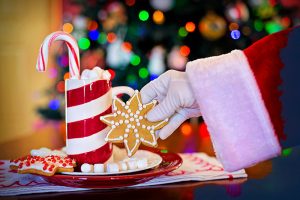 Santa Claus arm reaching for a star cookie. The cookie is on a plate with other cookies and mug of hot chocolate.