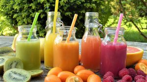 5 smoothies in green, orange and red. Surrounded by kiwi, orange and strawberries. 