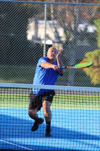 Senior in blue hitting ball over a net.