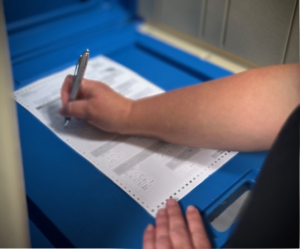 Blue ballot table showing just a person arms fill out a ballot with a pen.